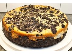 a cheesecake with chocolate chips on top sits on a white platter in front of a tile wall