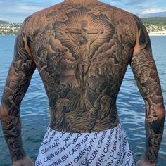 a man with tattoos on his back standing in front of the water