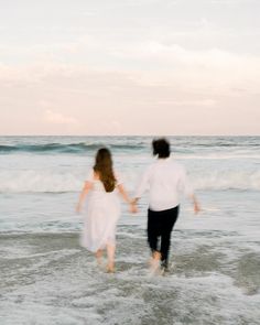 a man and woman are walking in the water at the edge of the beach holding hands