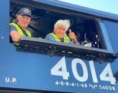 two men in safety vests giving thumbs up from the back of a train car