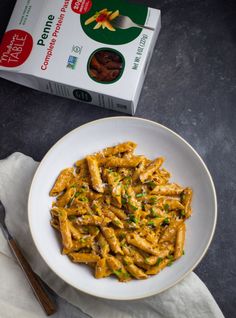 a white bowl filled with pasta next to a carton of pistachio cheese