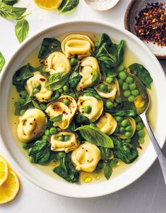 a white bowl filled with pasta, peas and spinach on top of a table