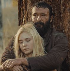 a man and woman standing next to each other in front of a tree with their eyes closed