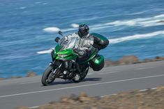 a man riding a green motorcycle down a road next to the ocean