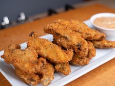 some fried food on a white plate with a small bowl of dipping sauce in the background