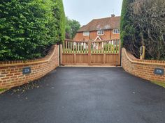 a gated driveway leading to a house with brick walls and trees on either side