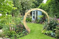 a garden with lots of flowers and plants around the area that has a circular wooden arch in it