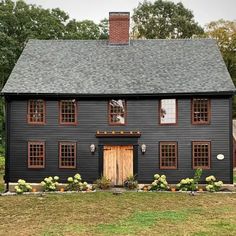 a black house with two windows and a wooden door in the front yard, surrounded by trees