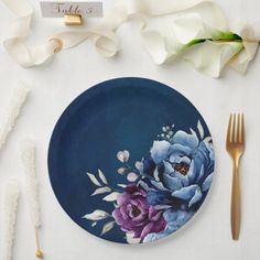 a blue plate with purple flowers on it next to gold forks and napkins,