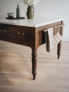 a vase with white flowers sitting on top of a wooden table next to a towel rack