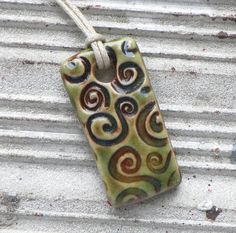 a ceramic tag hanging from a rope on the side of a building, with swirls painted on it