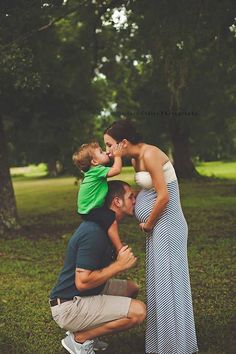 a man kneeling down next to a woman holding a child on his shoulders and kissing her cheek