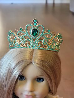 a doll with blonde hair wearing a green tiara and gold jewelry on it's head