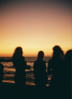 silhouettes of people standing on the beach at sunset