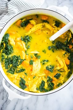 a white pot filled with yellow soup and spinach on top of a marble counter