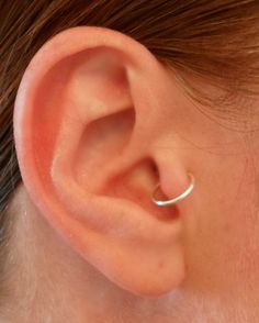 a woman's ear is shown with a thin silver nose ring