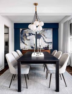 a dining room table with white chairs and a painting on the wall in the background