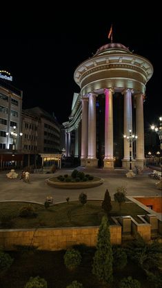 the building is lit up at night with colorful lights on it's pillars and columns