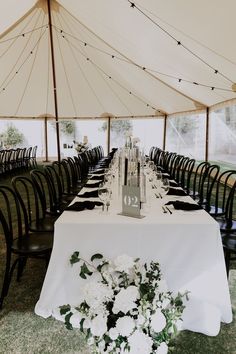 a table set up for an event under a tent with black chairs and white flowers