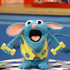 a blue stuffed animal sitting on top of a checkered table cloth with two yellow dumbs