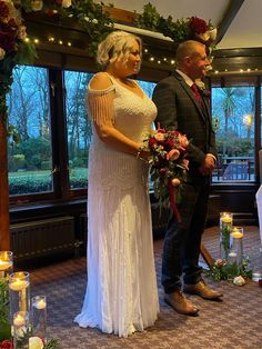 a man and woman standing next to each other in front of a window with candles