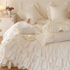 a bed with white ruffled sheets and pillows