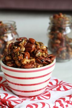 a bowl filled with nuts sitting on top of a red and white napkin next to two glass jars