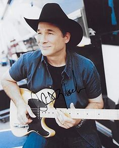 a man wearing a cowboy hat and playing an electric guitar in front of a boat