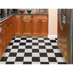 a black and white checkered floor in a kitchen with wooden cabinets, counter tops, and refrigerator