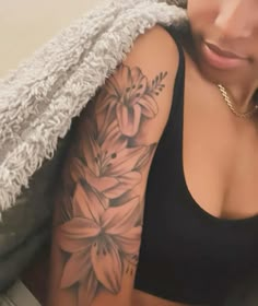 a woman with a flower tattoo on her arm and shoulder, sitting in front of a blanket