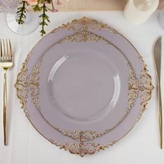 a white table with silverware and gold place settings on it, along with pink flowers