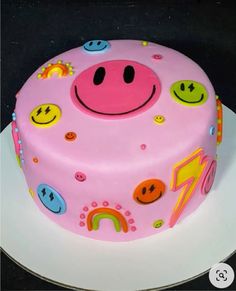 a pink birthday cake with smiley faces and rainbows on the frosting is sitting on a white plate