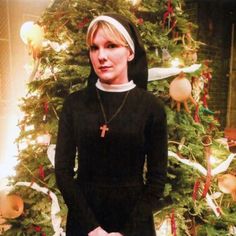 a woman standing in front of a christmas tree wearing a nun outfit and holding a cross