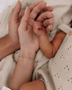 a person holding a baby's hand while laying on top of a white blanket