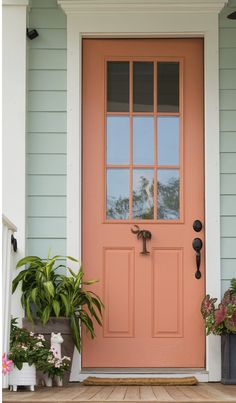 an orange front door with potted plants on the porch