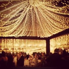 the inside of a tent is lit up with string lights and white tablecloths