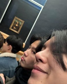 three young men sitting next to each other in front of a painting on the wall