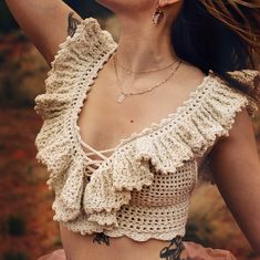 a woman with tattoos wearing a crochet top and holding her hair in the wind