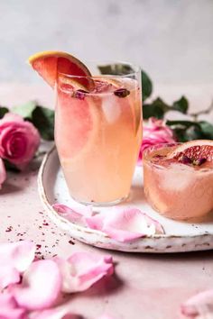 two glasses filled with pink wine and grapefruit on a plate next to flowers