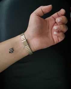 a woman's arm with a gold bracelet on it and a small black letter tattoo