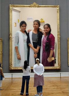 three women standing in front of a large mirror