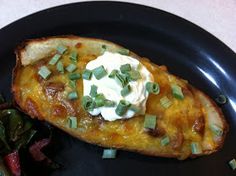 a black plate topped with an enchilada and greens covered in sour cream