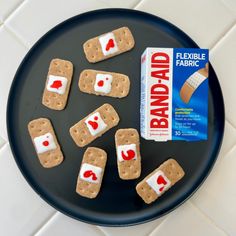 a black plate topped with cookies and marshmallows next to a carton of bandages