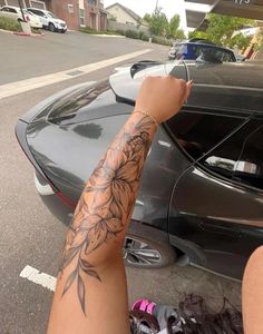 a person with a tattoo on their arm next to a parked car in a parking lot