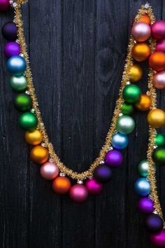 an assortment of colorful christmas ornaments on a black background with gold chains and beads hanging from them