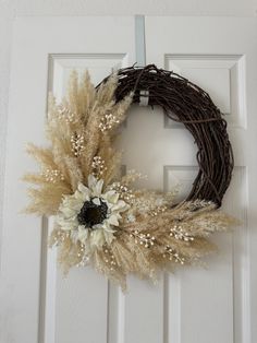 a wreath with dried grass and flowers hanging on the front door to give it a rustic look