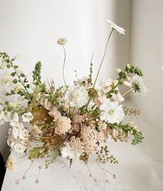 a vase filled with lots of flowers on top of a white counter next to a window