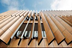 an upward view of a tall building with wooden panels on it's sides and windows