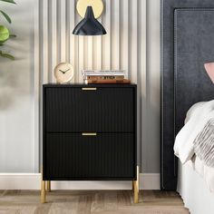 a nightstand with a clock on it next to a bed