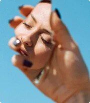 a woman with her eyes closed is holding her hand up to her face and looking at the sky